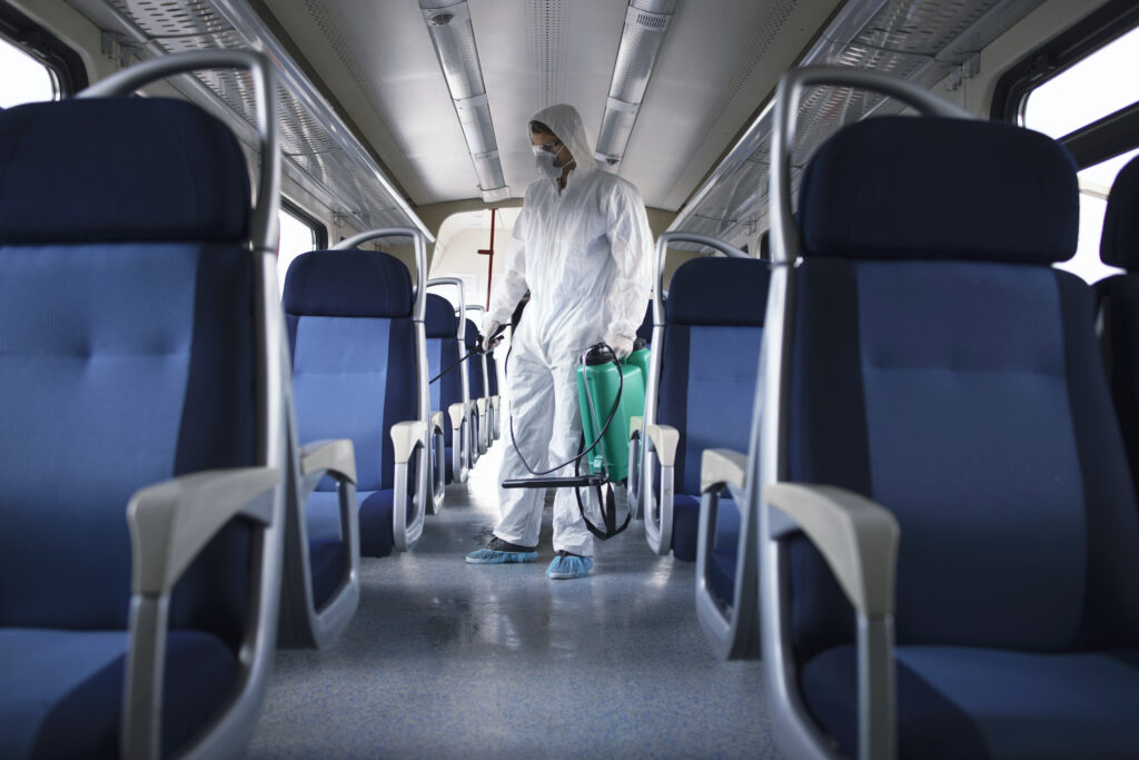 Man in white protection suit disinfecting and sanitizing subway train interior to stop spreading highly contagious corona virus.