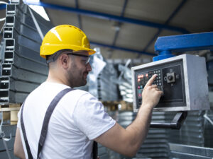 Factory worker operating industrial machine and setting parameters on the computer.
