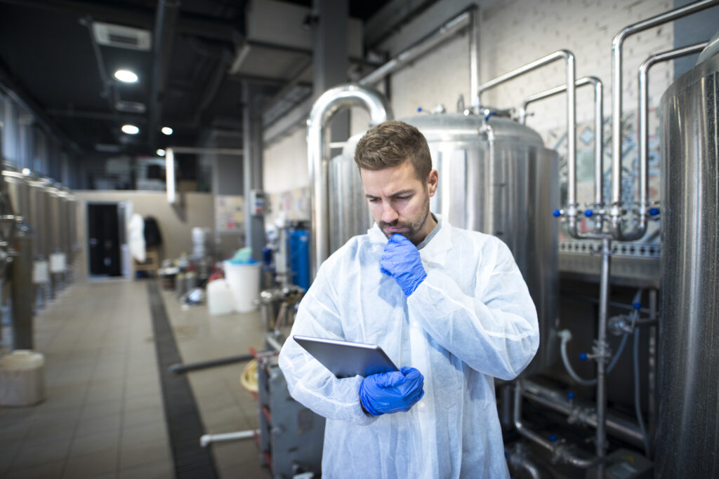 Technologist reading production reports on tablet computer in factory.