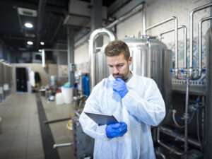 Technologist reading production reports on tablet computer in factory.