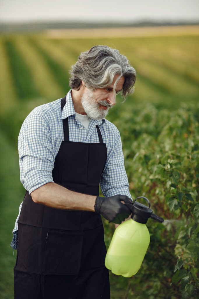 Senior man watering his plants in his garden with sprinkle